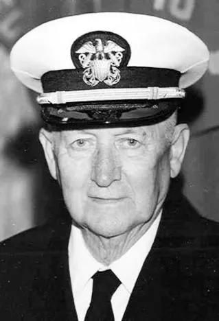 Elderly man in a naval uniform and cap with an emblem, posing for a portrait.